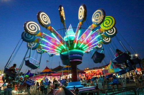 Colorful illuminated swing ride at a carnival at dusk, with riders on swinging seats and bright spiraled decorations around a central column.